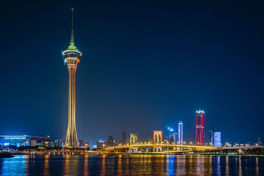 Captivating night scene of Macau Tower with illuminated skyline and bridge reflections.